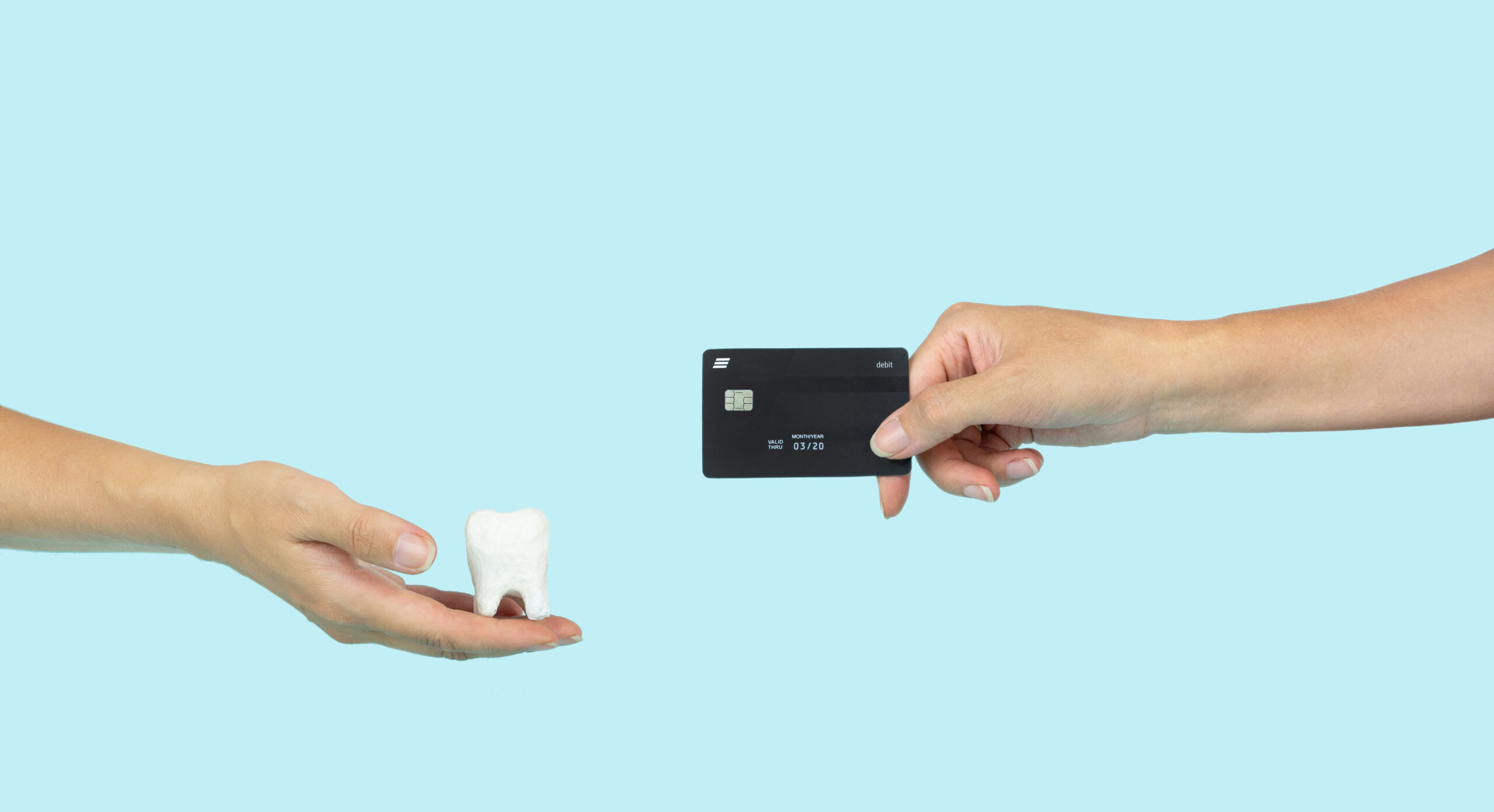 Two hands holding a tooth and a credit card to demonstrate the exchange of dental care for money.