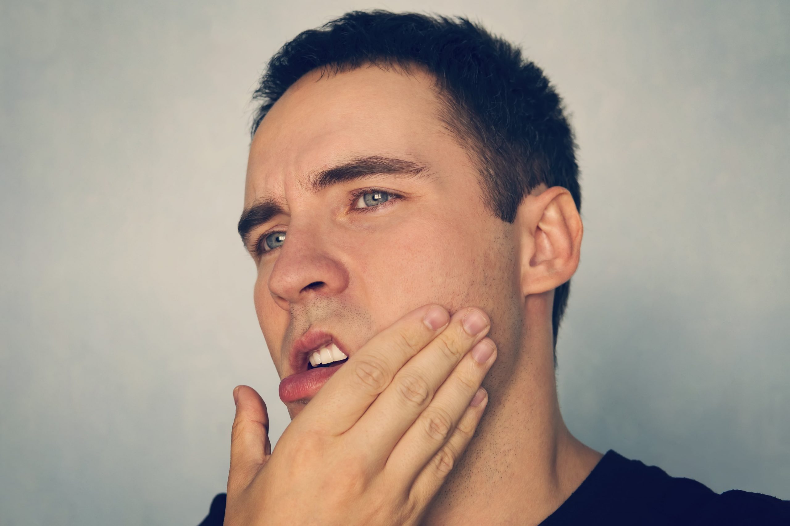 Man with jaw pain pressing hand to face.